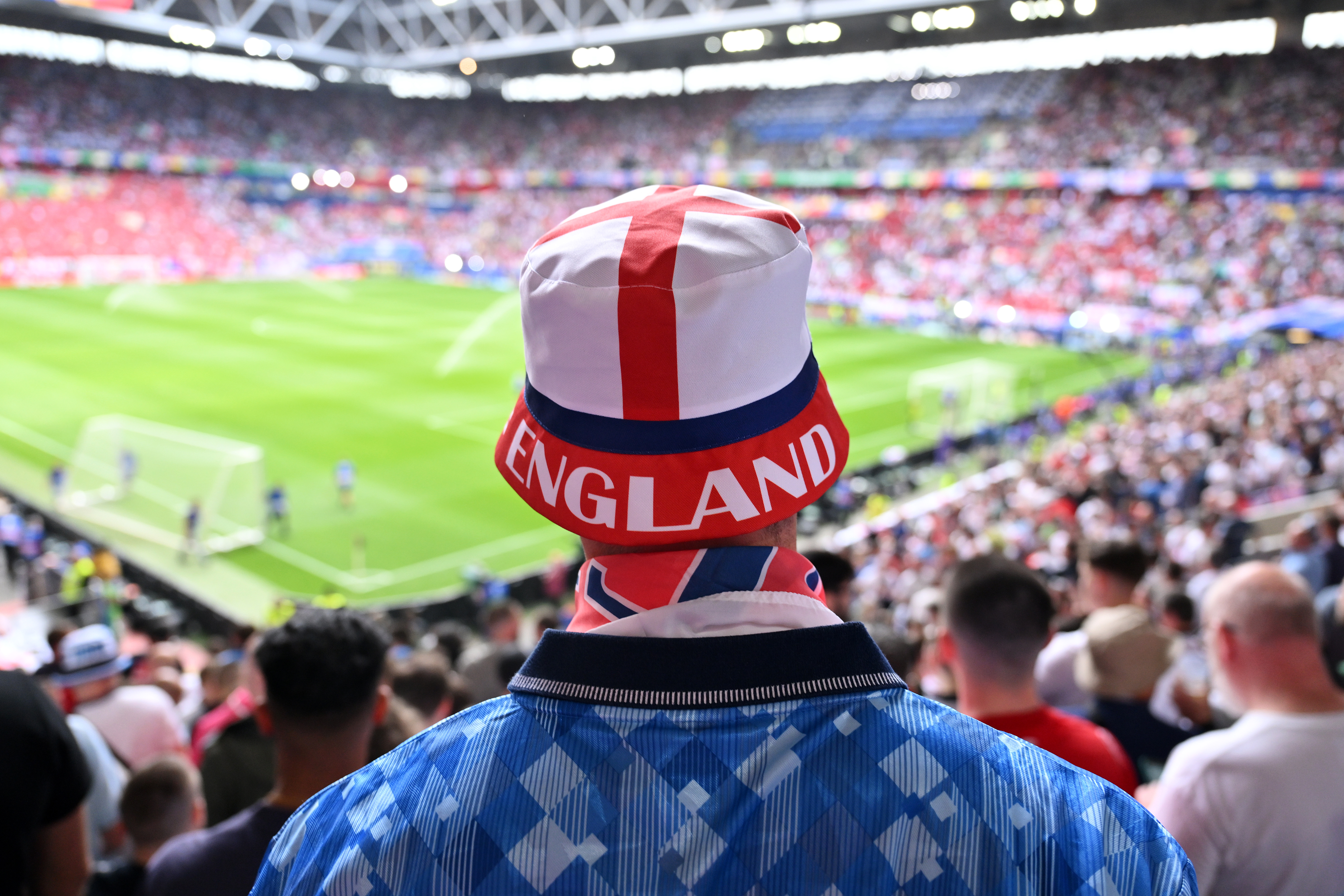 Un aficionado con un sombrero de pescador inglés observa un partido de fútbol desde las gradas.