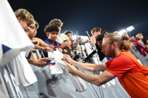 Un jugador de fútbol firma una camiseta para los aficionados (© Howard Smith/ISI Photos/USSF/Getty Images)