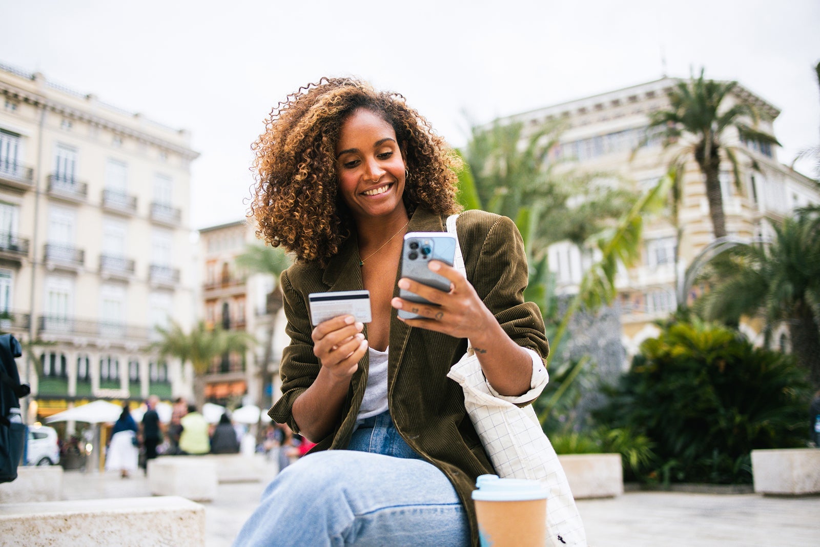 Mujer feliz disfrutando de un café en la calle y comprando en línea