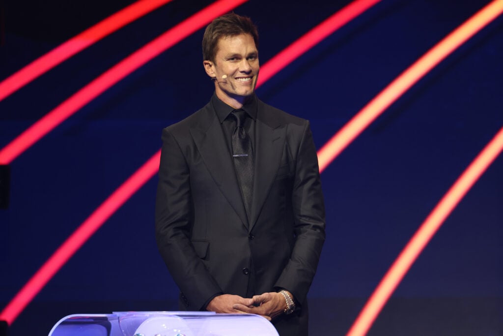 El asistente Tom Brady reacciona ante John F. en el escenario del sorteo oficial de la Copa Mundial de la FIFA 2026 en el Kennedy Center.